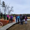 Na zdjęciu 11 osób z kijkami do nordic walking. Osoby pozują stojąc przy jazie na Jeziorze Krutyńskim