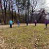 Grupa 6 osób wykonująca ćwiczenia z kijkami nordic walking na polanie przy Jeziorze Mokrym.