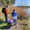 Dwie osoby, kobieta i mężczyzna stoją nad brzegiem stawu, obok nich worek wypełniony śmieciami.