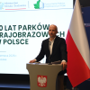 Prelegent wygłasza wystąpienie podczas konferencji „50 lat parków krajobrazowych w Polsce” na tle ekranu z nazwą wydarzenia oraz flag Polski i Unii Europejskiej.