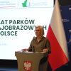 Prelegentka przemawia podczas konferencji „50 lat parków krajobrazowych w Polsce” na tle ekranu z nazwą wydarzenia oraz flag Polski i Unii Europejskiej.